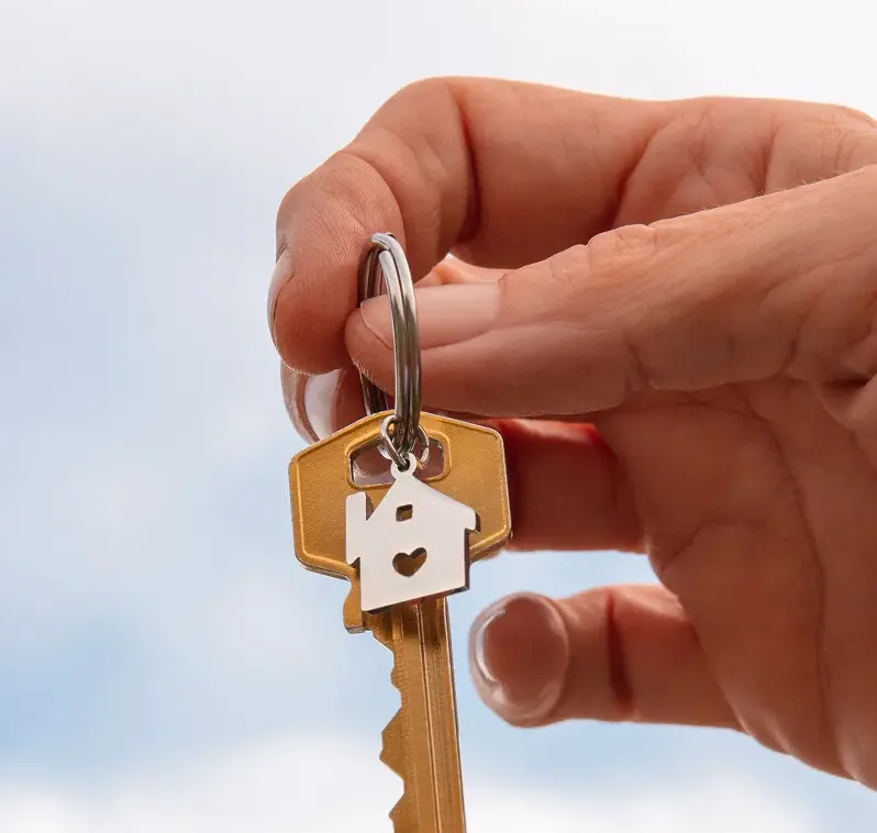 Mão segurando a chave de casa com chaveiro de casinha: a chave do primeiro imóvel