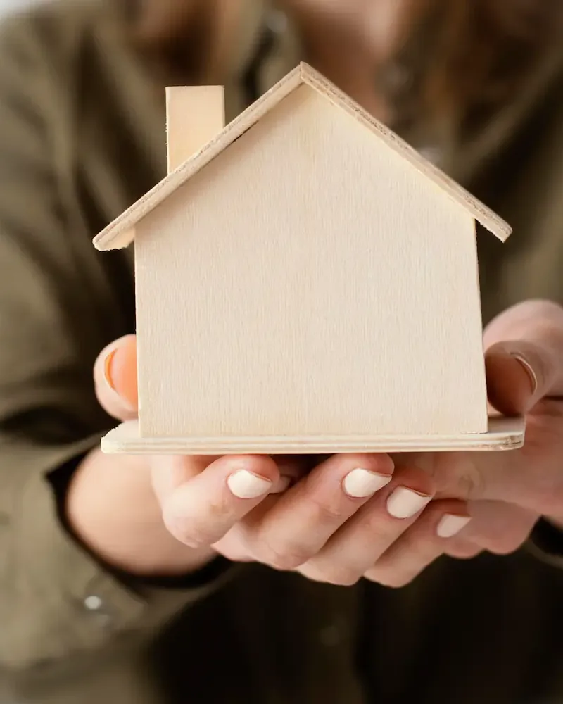 Mãos segurando uma casinha de madeira: o sonho da casa própria