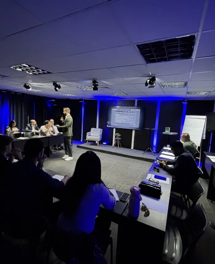 Flávio Ribeiro de pé, conduzindo uma aula para uma turma numa sala com luz azul