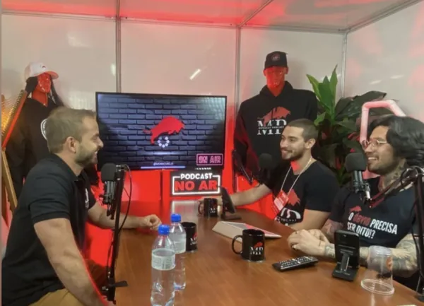 Flávio Ribeiro conversando com convidados num estúdio de podcast com luz vermelha