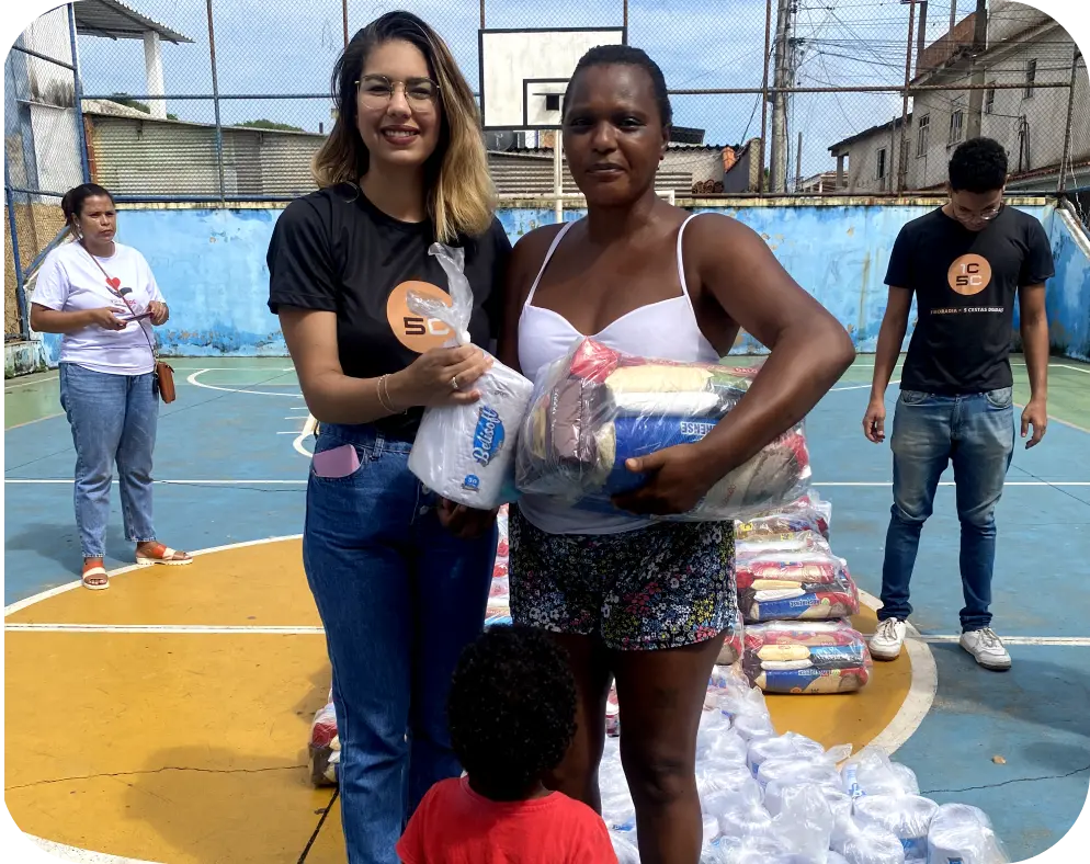 Corretora da FR Prime entregando cesta básica do 1C5C a uma moradora na quadra