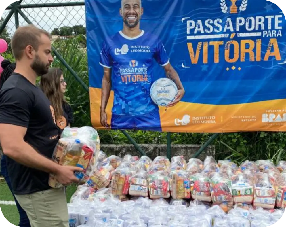 Flávio Ribeiro carregando cesta básica diante da faixa do Passaporte para a Vitória