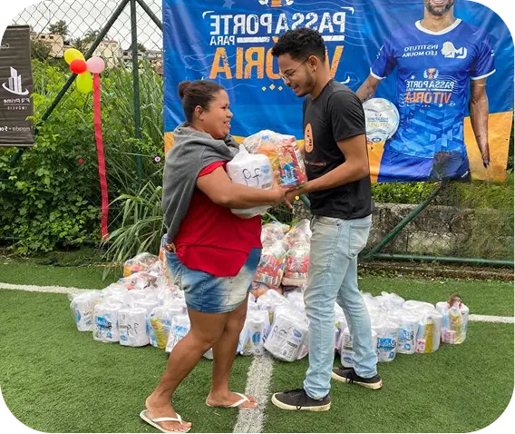 Corretor da FR Prime entregando cesta básica a uma moradora no campo do Passaporte para a Vitória