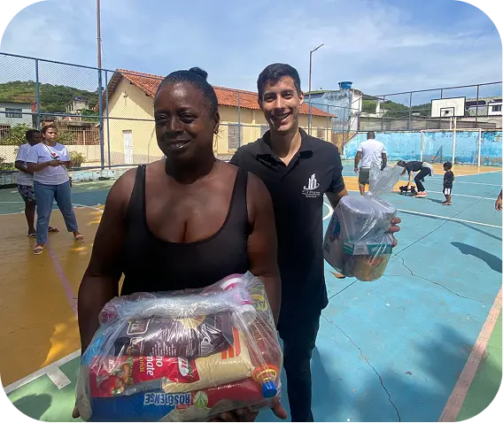 Moradora recebendo cesta básica do 1C5C na quadra, ao lado de um corretor da FR Prime